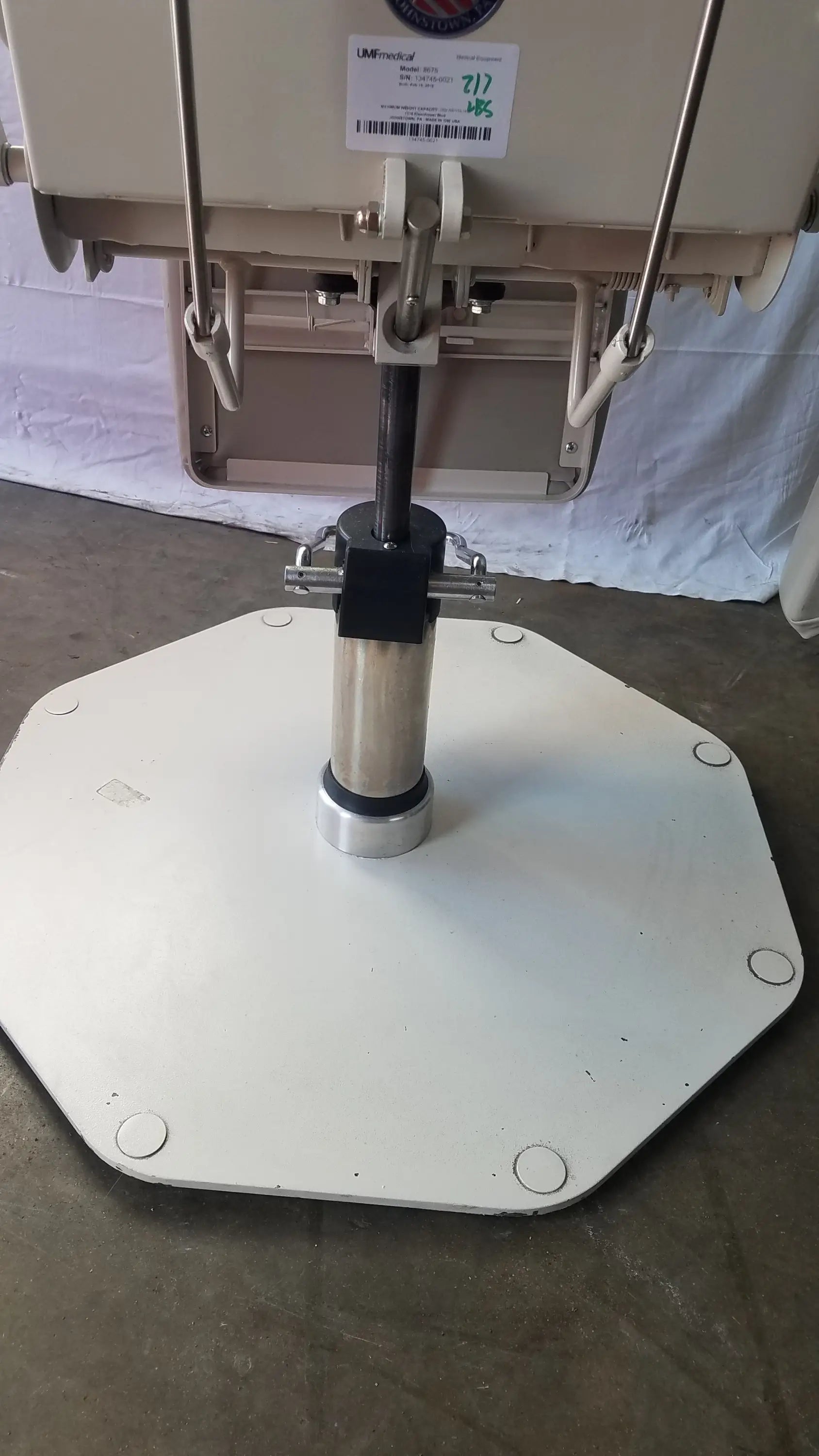 White octagonal base with central metallic cylinder and black mounting hardware of UMF Medical adjustable phlebotomy chair