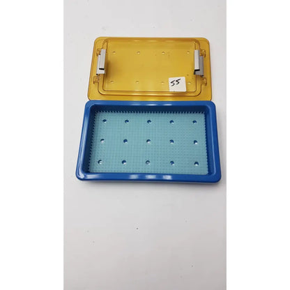 Blue and yellow plastic universal instrument sterilization container with finger matt and grid of holes in base