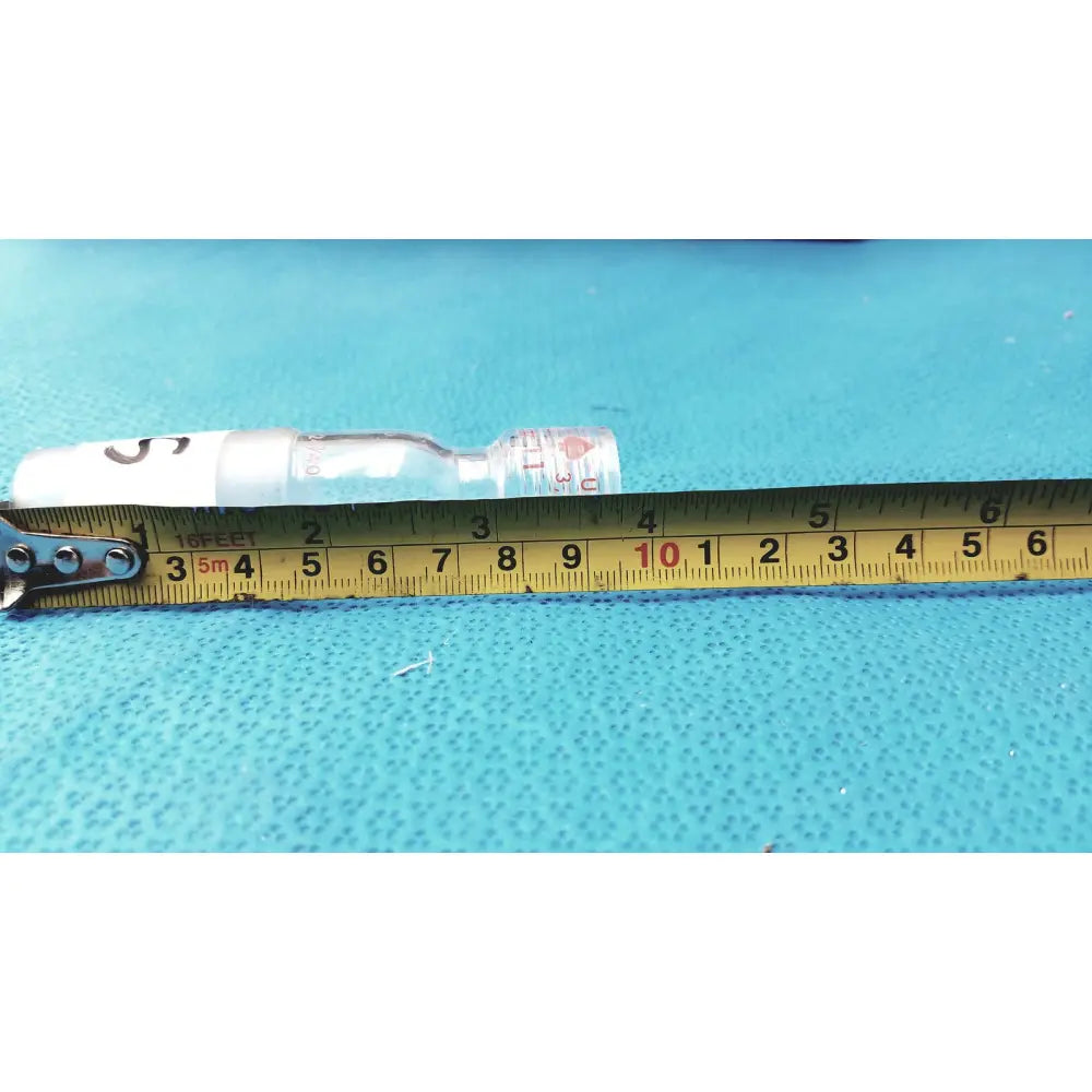 Clear glass thermometer adapter vial with white cap and red label lying next to yellow measuring tape made in usa