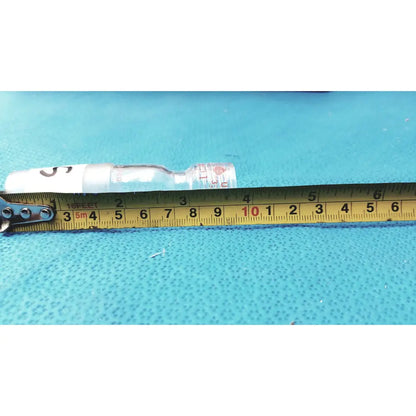 Clear glass thermometer adapter vial with white cap and red label lying next to yellow measuring tape made in usa