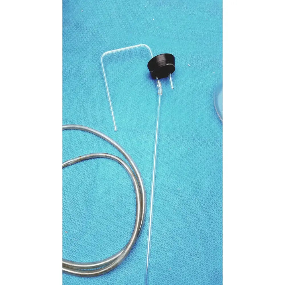 Black cylindrical sensor with two metallic pins and flexible tube resting on blue surface beside vintage clear glass bottle with embossed base