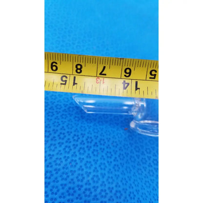 Vintage 9 inch clear glass bottle with embossed base and narrow neck positioned horizontally beneath yellow measuring tape