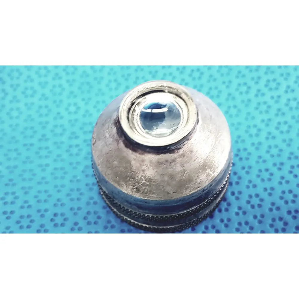 A weathered silver-toned metal lens cap with glass insert and ridges for volk super quad ophthalmic laser lens