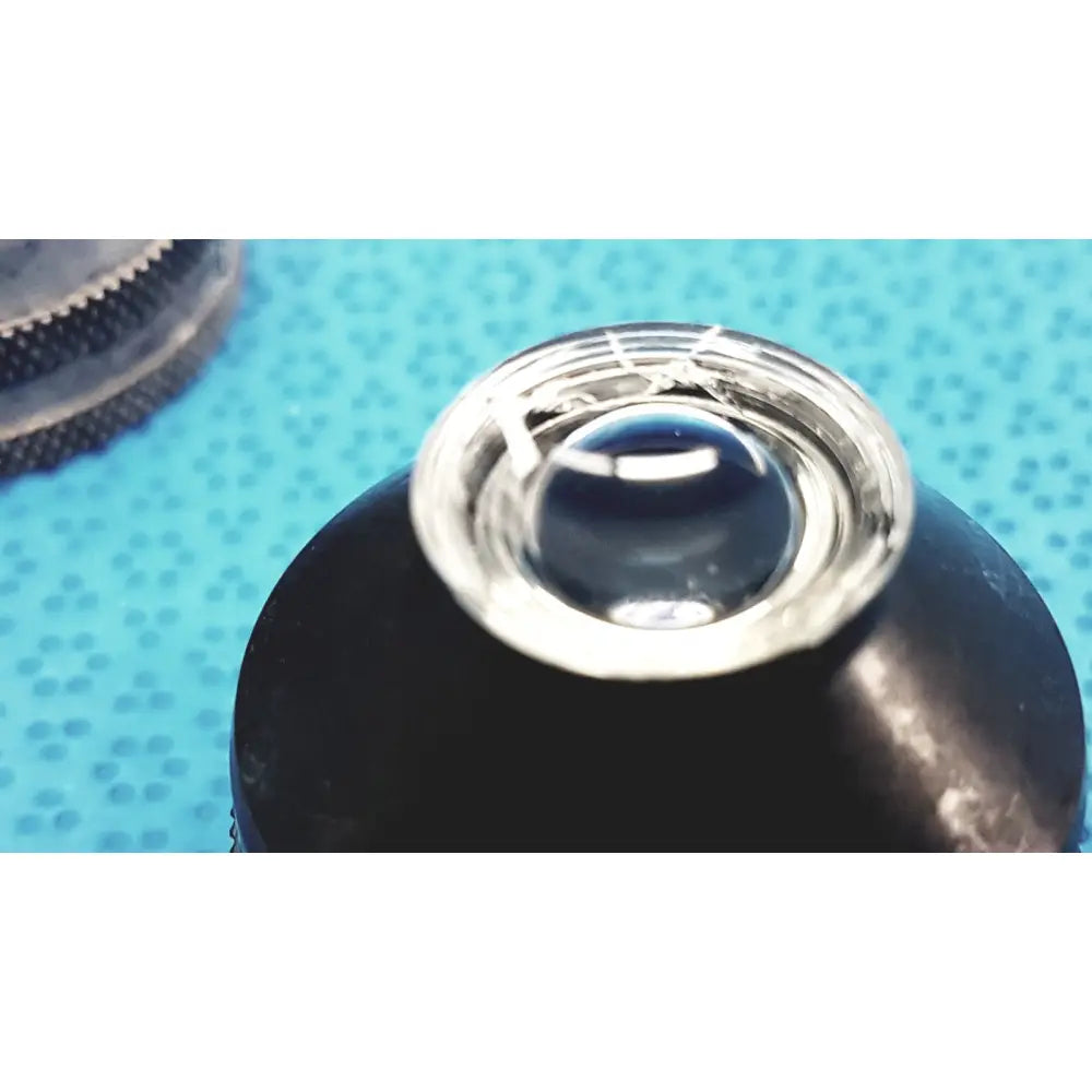 Silver-rimmed volk super quad ophthalmic laser lens resting on a black textured surface for precision eye surgery