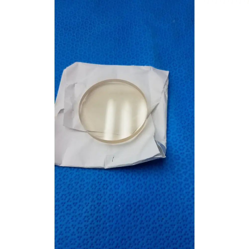 Clear circular glass lens w1147 schott zerodur exp class 2 127x90mm resting on crumpled white paper wrapper