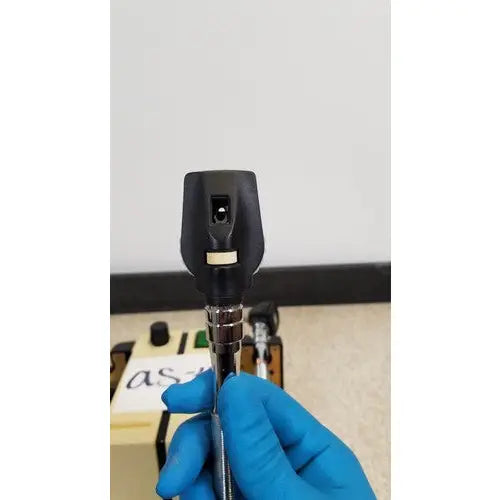 Welch allyn transformer otoscope ophthalmoscope with black head and metallic shaft held in blue gloves visible