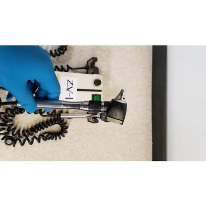 Welch Allyn 74710 wall transformer with black and silver otoscope and coiled cord held by a gloved hand for reuse medical use