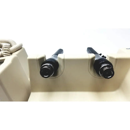Two black cylindrical welch allyn series transformer otoscope and ophthalmoscope devices mounted in beige holder