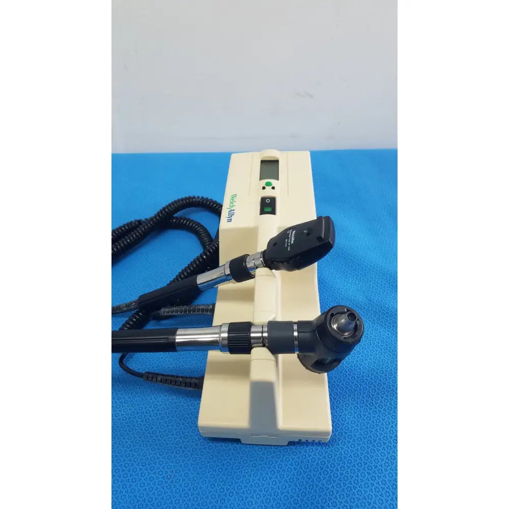Beige hoya alpha ophthalmoscope with black and silver arms digital display and coiled cables in welch allyn series transformer for reuse medical use