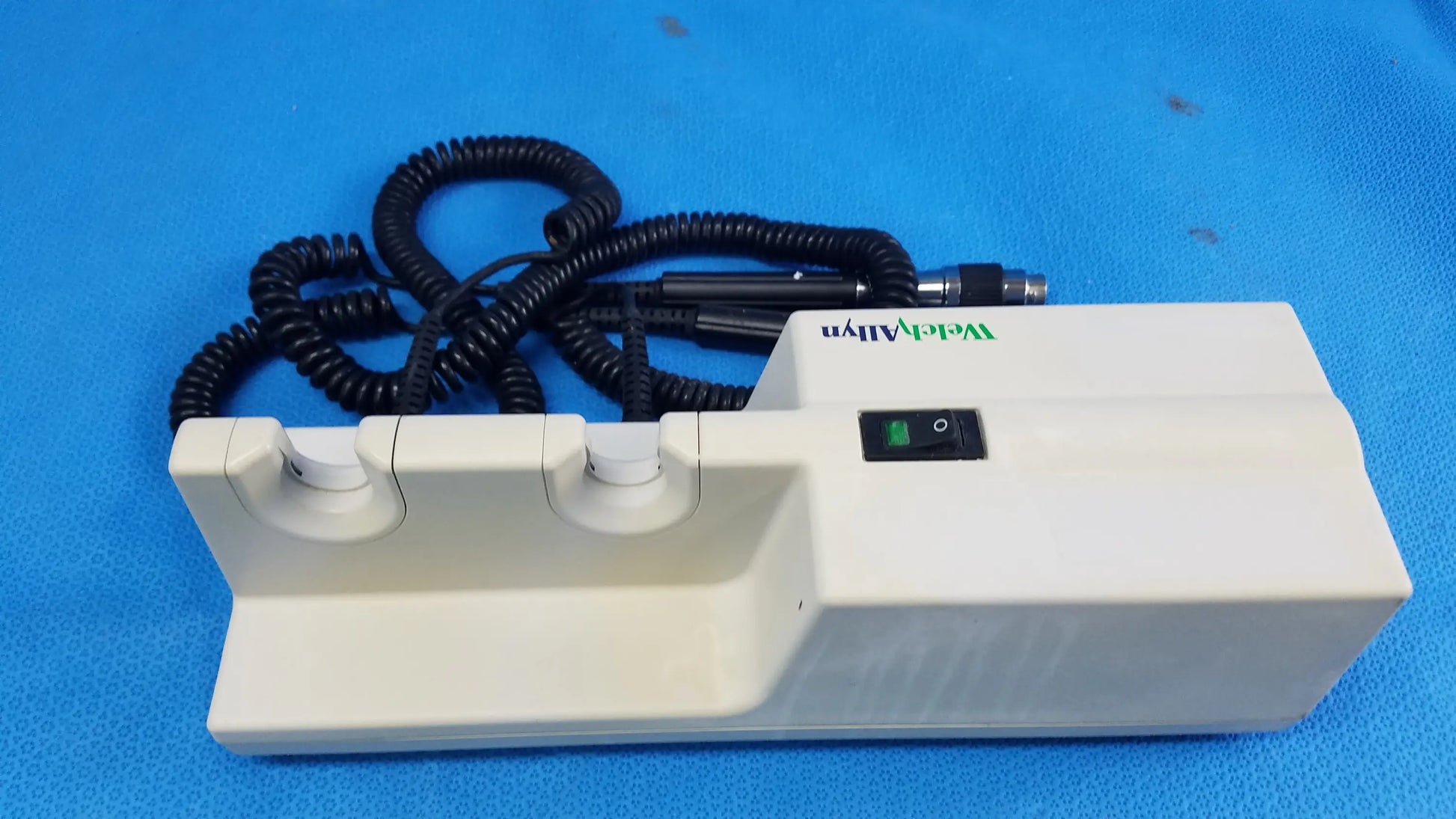 White plastic welch allyn 767 series transformer base with black coiled cord and green switch for wall-mounted diagnostic power without instrument heads