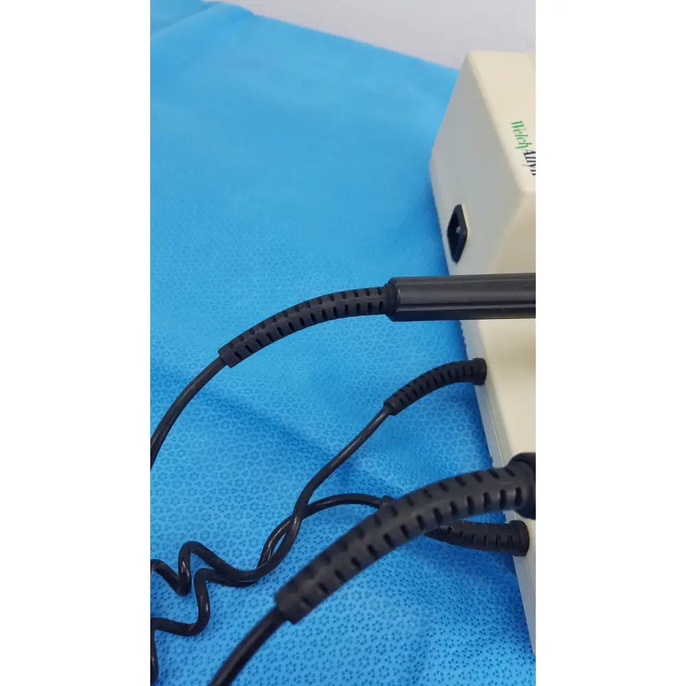 Black coiled cables with ribbed protective sleeves connected to the back of a beige welch allyn 767 series wall transformer