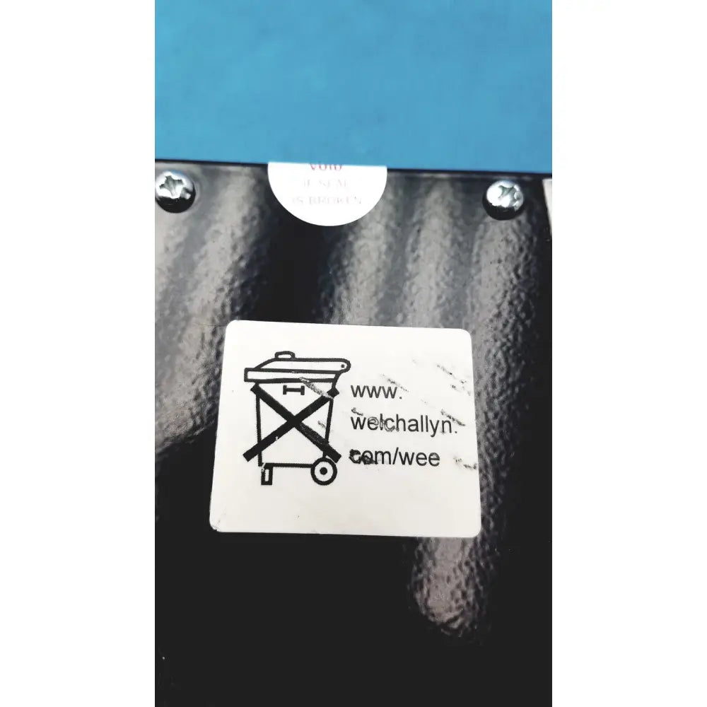 Black textured surface on the back of welch allyn 9600 plus calibration tester with a white sticker and plus calibration icon