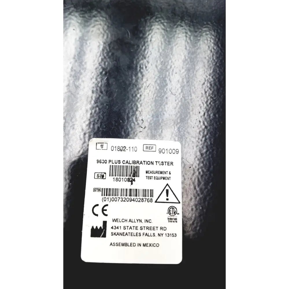 White rectangular label on the back of welch allyn 9600 plus calibration tester with black text and plus calibration tester info