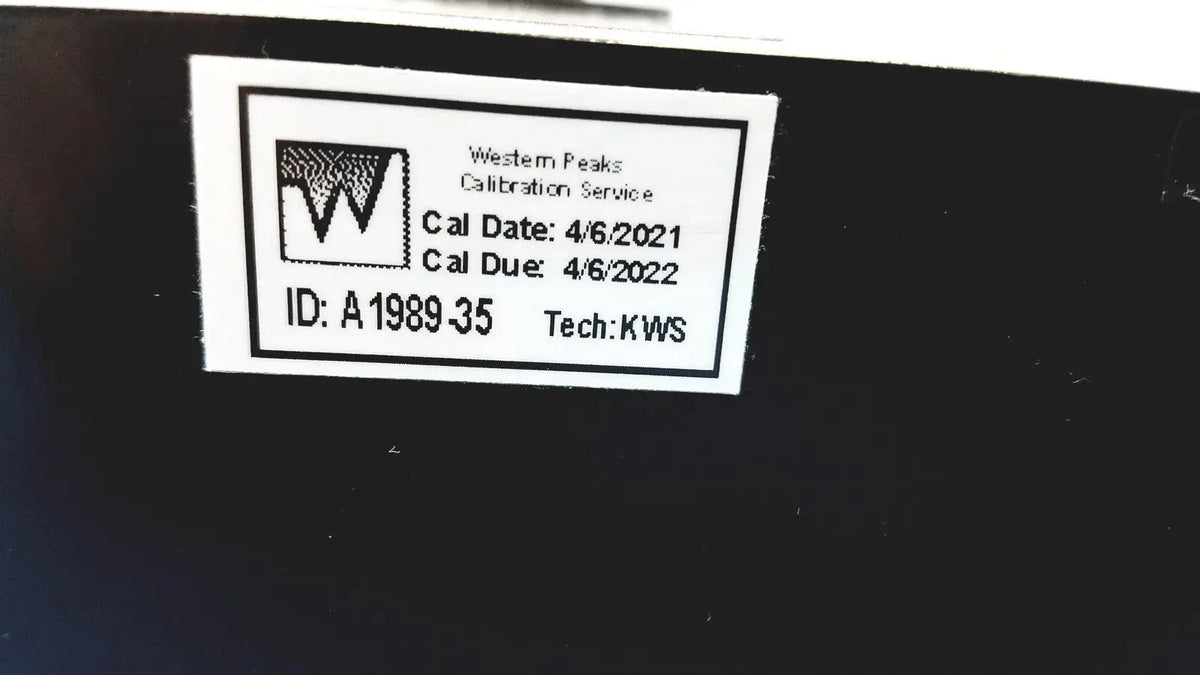 White rectangular calibration label with black text and logo on dark surface for welch allyn 9600 plus calibration tester