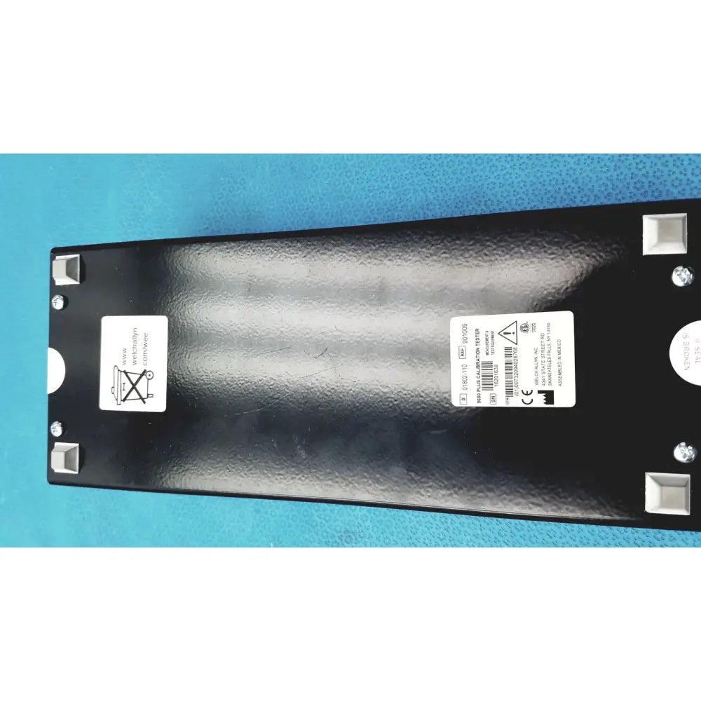 Black textured plastic panel with white labels and silver screws on the back of welch allyn 9600 plus calibration tester