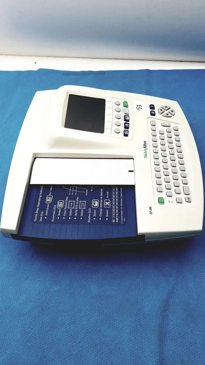 White welch allyn cp200 ekg monitor with small screen gray keypad and blue paper tray labeled widal 53 for ecg recording