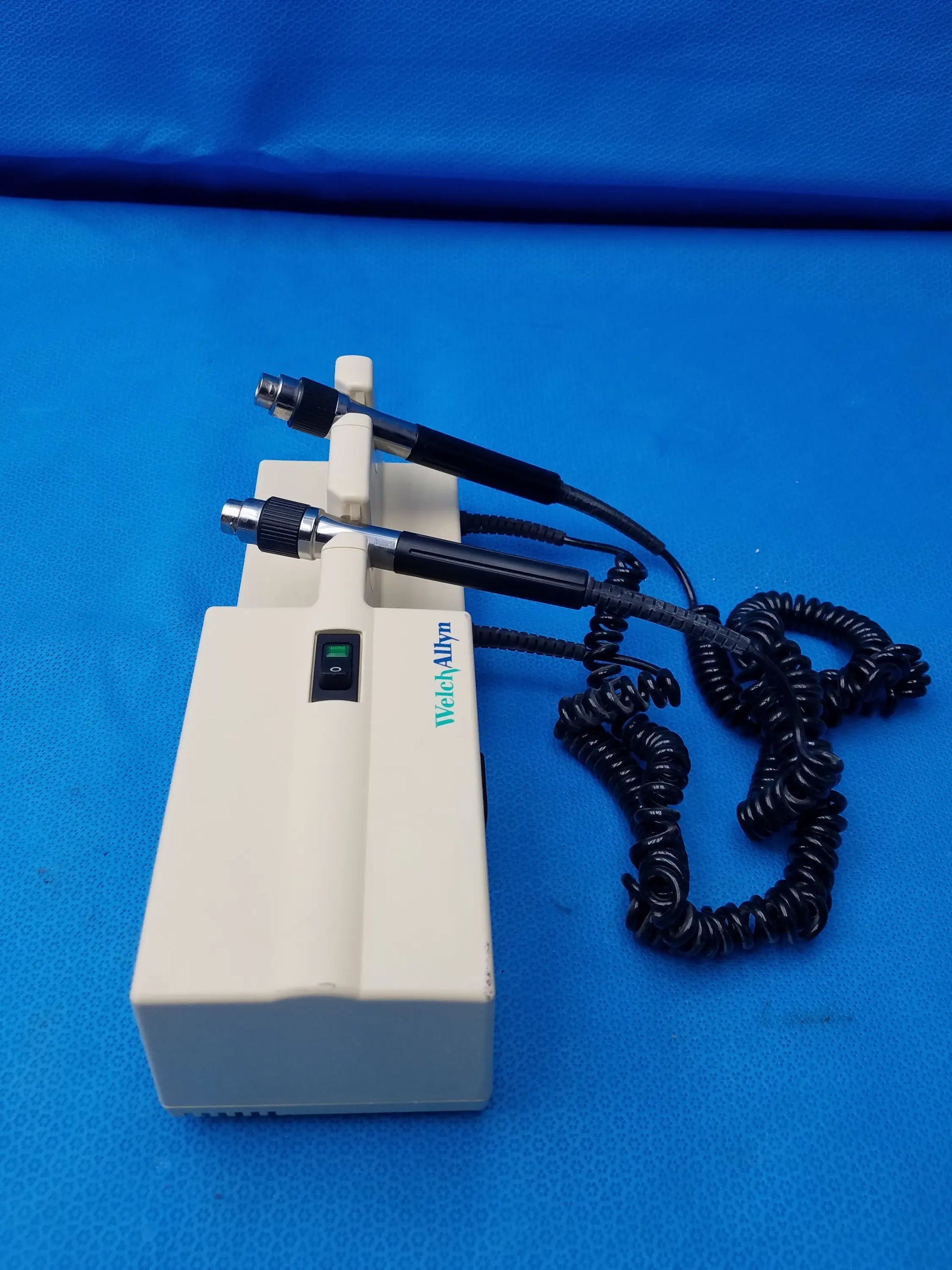 Cream-colored Welch Allyn diagnostic wall transformer with two black-handled probes and coiled black cable no heads