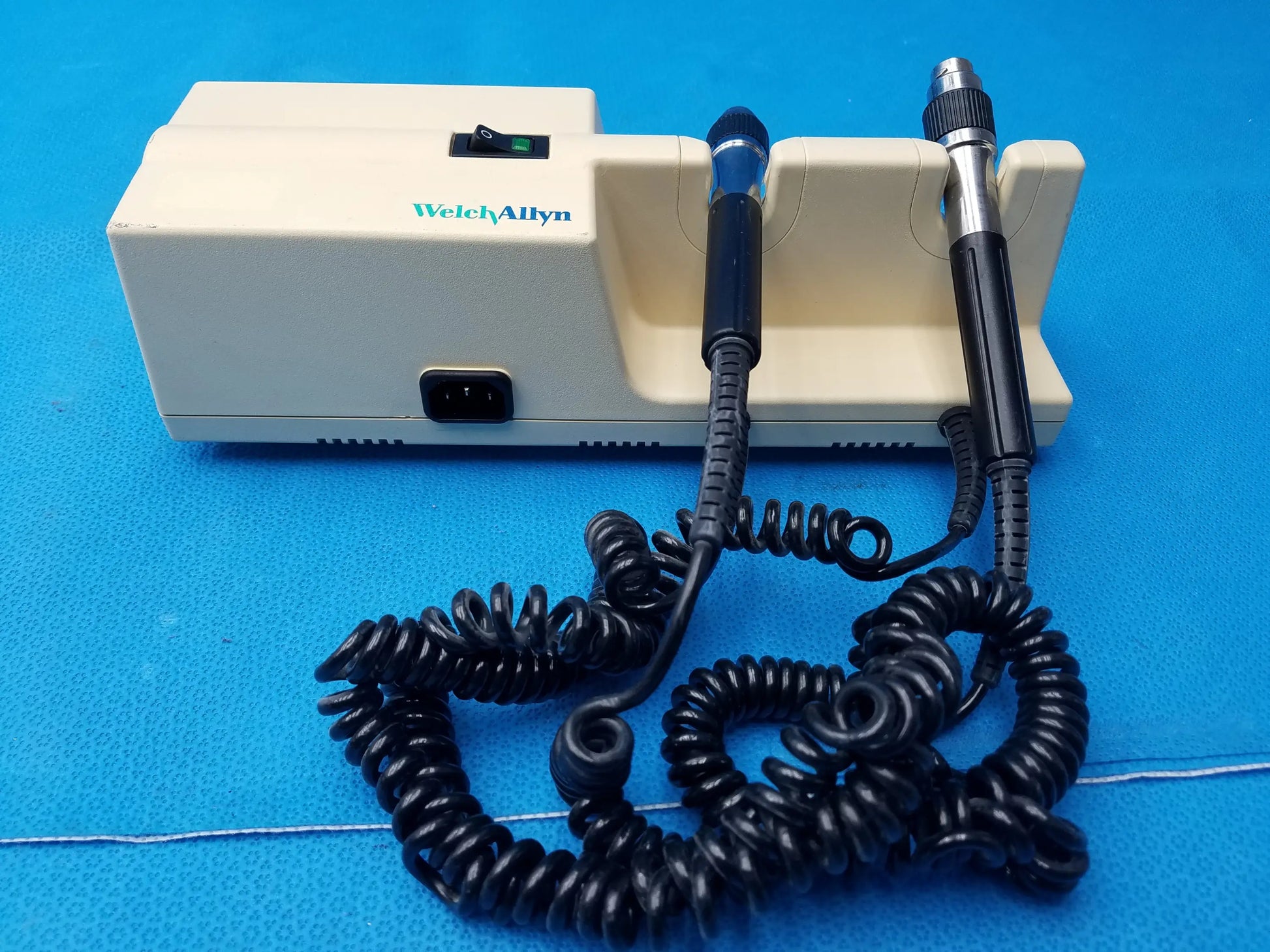 Cream-colored welch allyn diagnostic wall transformer with two black-handled probes and coiled black cords no heads