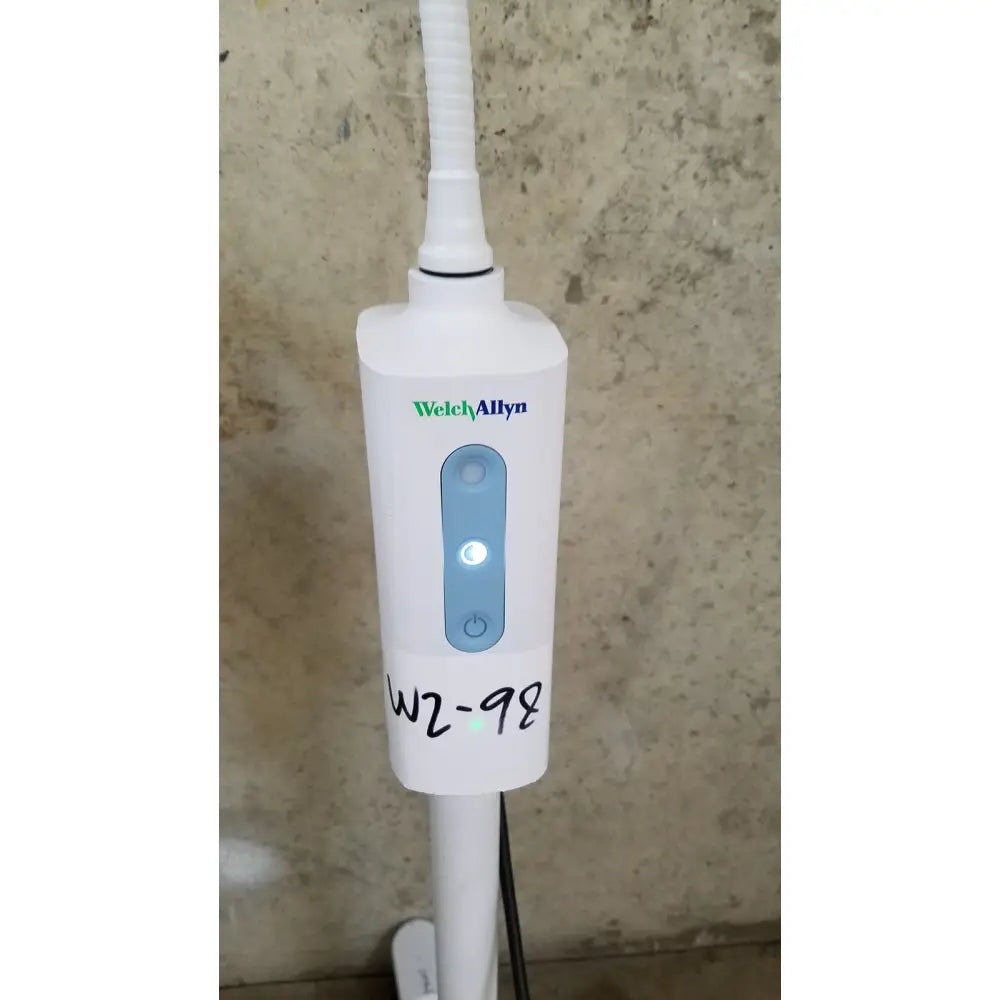 White welch allyn exam light with blue illuminated power button and rolling stand marked w2 98 on its side