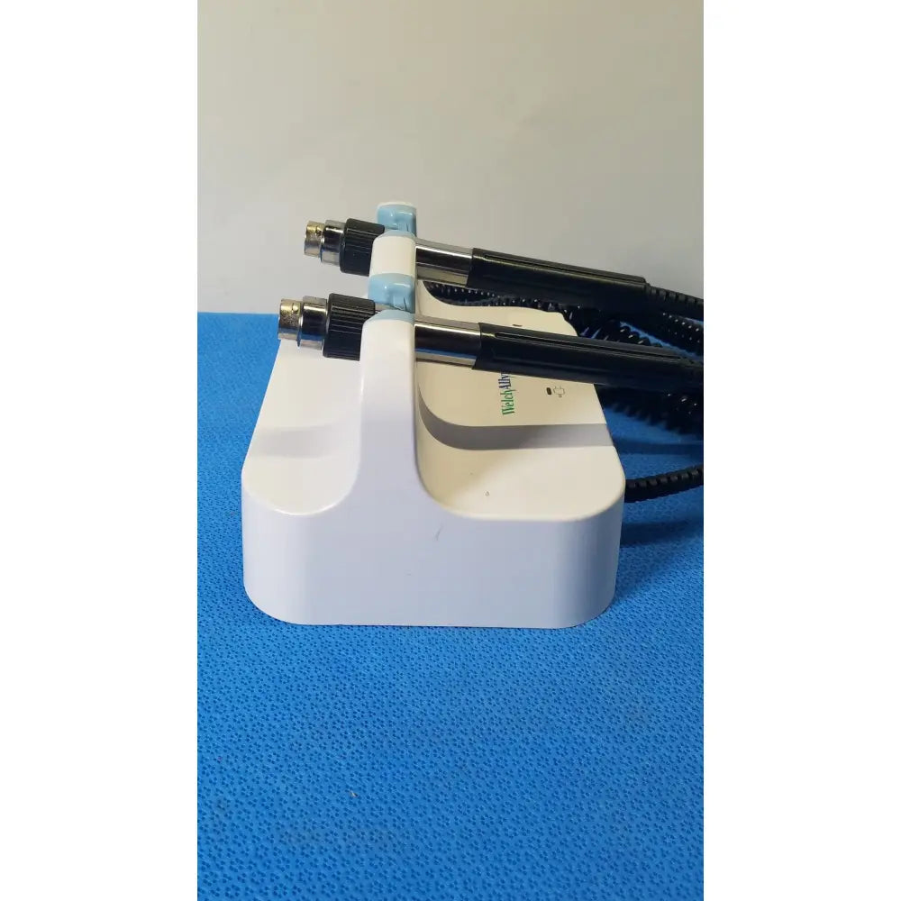 Welch allyn white plastic medical wall transformer stand holding two black and light blue handheld examination tools