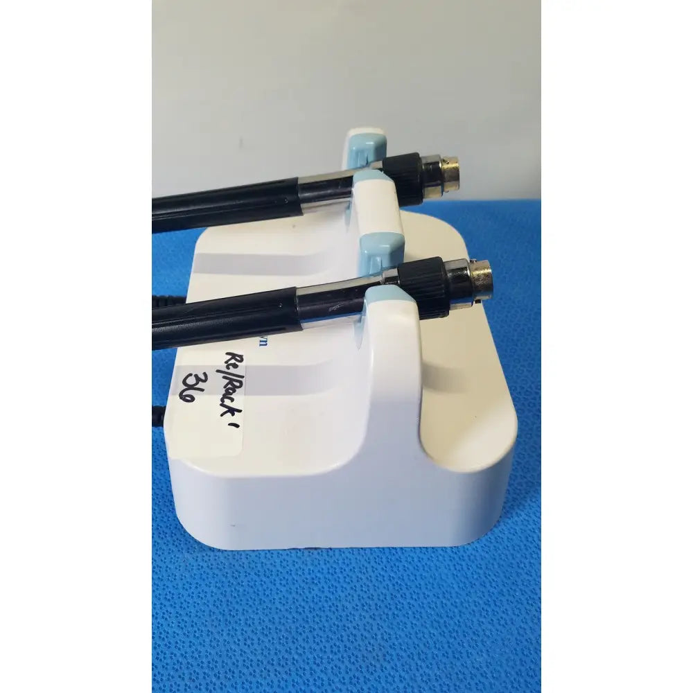 White plastic stand holding two black welch allyn medical-grade endoscopes with metallic connectors and coiled cords on wall transformer