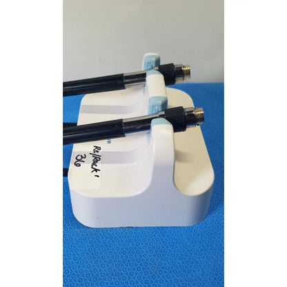 White plastic stand holding two black welch allyn medical-grade endoscopes with metallic connectors and coiled cords on wall transformer