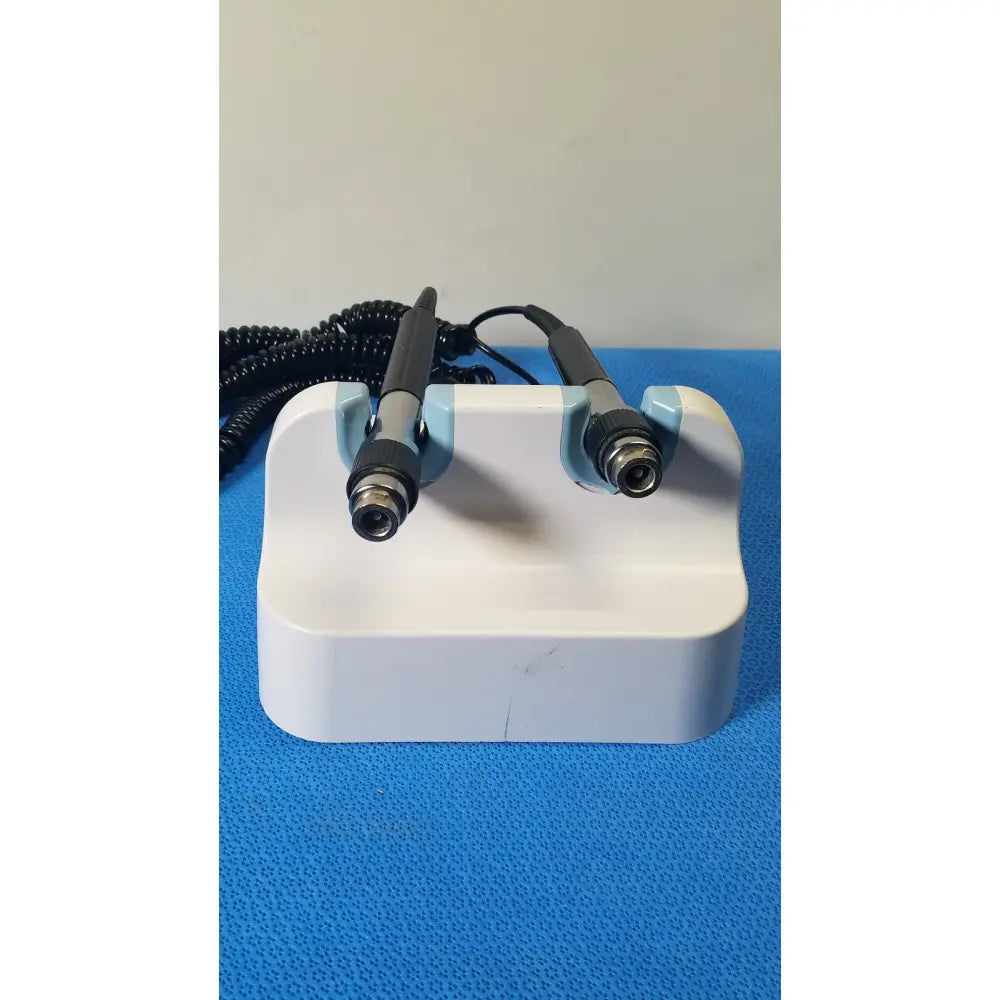 White plastic stand holding two black and silver handheld welch allyn wall transformer medical devices with coiled cords