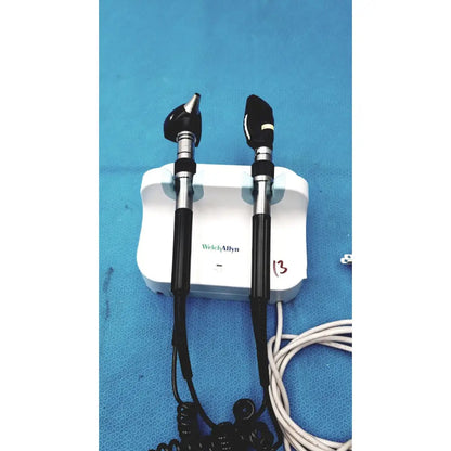 Welch allyn wall transformer with black and silver otoscope handles mounted on a white charging base for reuse medical use