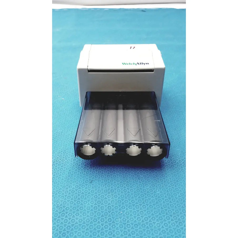 White and black welch allyn universal 17 battery charger with transparent tray holding four cylindrical batteries for universal kleenspec single use