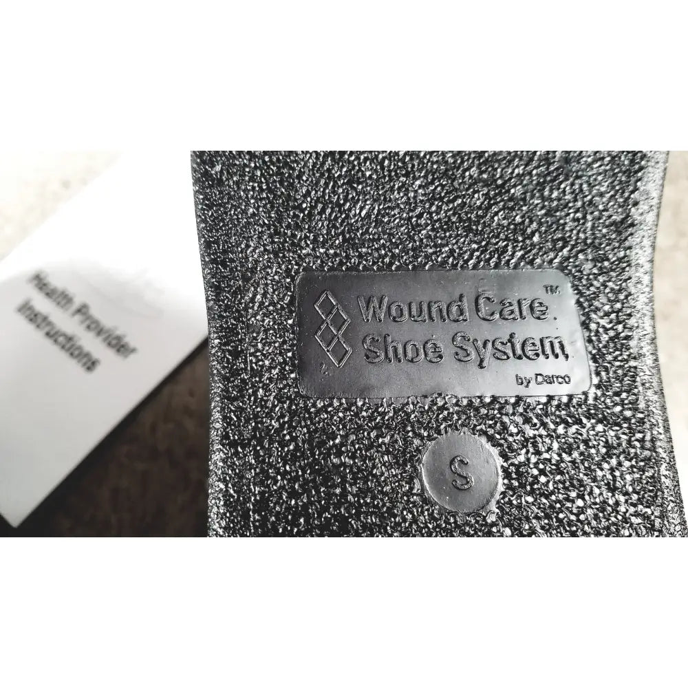 Silver metallic label on textured black fabric wound care shoe insert reading wound care shoe system by darco small