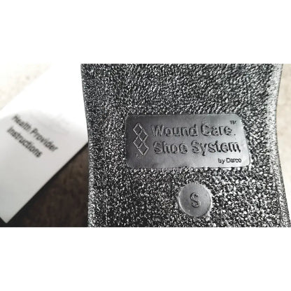 Silver metallic label on textured black fabric wound care shoe insert reading wound care shoe system by darco small