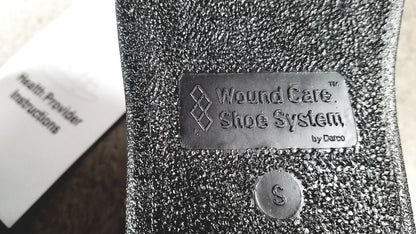 Silver metallic label on textured black fabric wound care shoe insert reading wound care shoe system by darco small