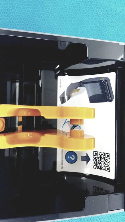 Yellow plastic clamp holding a black device with qr code label on the back of a zebra zd620 thermal transfer desktop printer