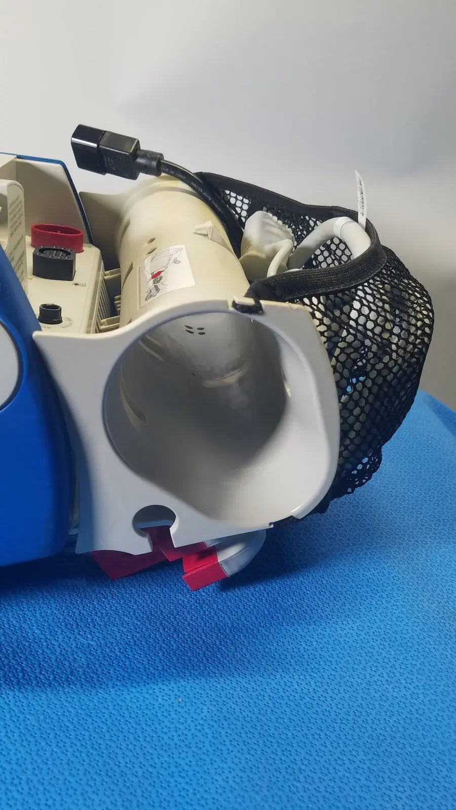 Blue and white electric vacuum cleaner with black mesh carrying bag attached shown alongside zoll r series als patient monitor