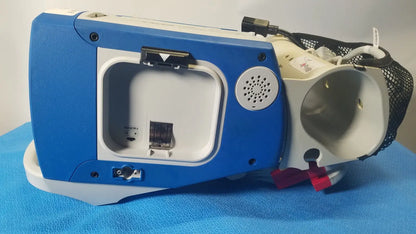 Blue and white portable oxygen concentrator with mesh tubing compartment on the back of zoll r series als patient monitor