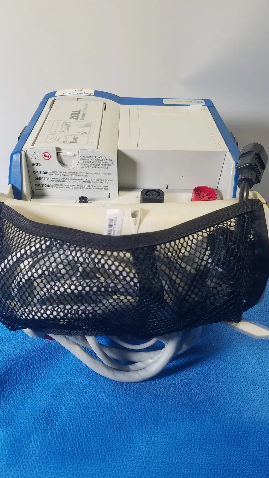 Blue and white zoll r series als patient monitor with black mesh pouch and surepower battery pack attached front